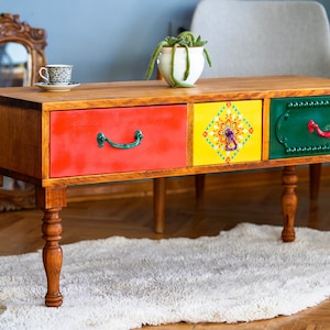 May include: A wooden coffee table with three drawers. The drawers are painted in bright colours: red, yellow and green. The table has turned wooden legs.