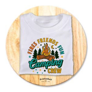 Könnte beinhalten: Weißes T-Shirt mit einem Retro-Camping-Design mit einem Lagerfeuer, Bäumen und dem Text "Fires Friends Fun Camping Crew".