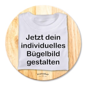 Könnte beinhalten: Weißes T-Shirt mit dem Text "Jetzt dein individuelles Bügelbild gestalten" in Schwarz bedruckt. Der Text ist mittig auf dem Shirt platziert. Das Shirt liegt auf einer Holzoberfläche. Der Text "Printrebel" ist in Schwarz auf der Unterseite des Shirts aufgedruckt.