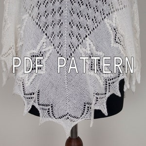 May include: White crocheted shawl with a lacy pattern. The shawl is displayed on a black mannequin. The text "PDF PATTERN" is printed on the shawl.