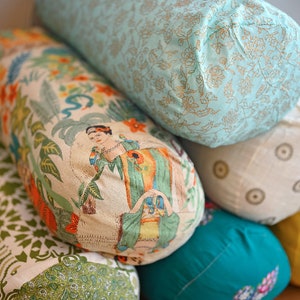 May include: A stack of six colourful cylindrical cushions with various floral patterns. The cushions are made of fabric and have a soft, comfortable texture.