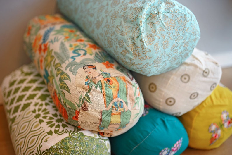 May include: A stack of six colourful cylindrical cushions with various floral patterns. The cushions are made of fabric and have a soft, comfortable texture.