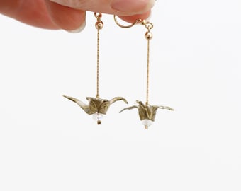 May include: Gold dangle earrings with a green origami crane charm on each earring.