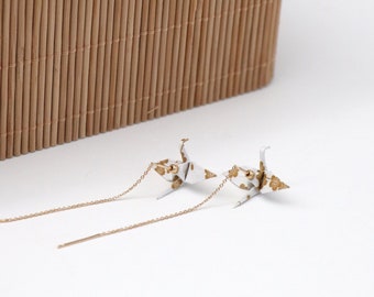 May include: A pair of gold chain earrings with white origami cranes with gold accents. The cranes are hanging from the chains.