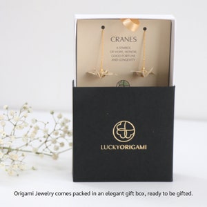 May include: A black gift box with a gold logo that says "LUCKYORIGAMI". Inside the box are gold origami crane earrings. The box has a white lid with a card that says "CRANES A SYMBOL OF HOPE, HONOR, GOOD FORTUNE AND LONGEVITY".
