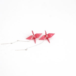 May include: A pair of pink origami crane earrings with silver chains. The earrings are hanging from silver posts.