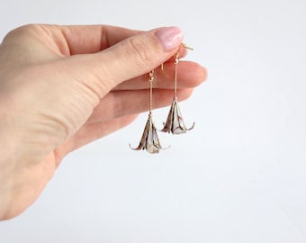 May include: A pair of gold dangle earrings featuring origami paper flowers. The flowers are white with pink and gold accents.