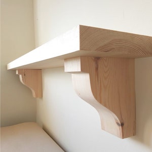 May include: A natural wood shelf with two decorative brackets. The shelf is made of unfinished pine wood and is ready to be stained or painted.