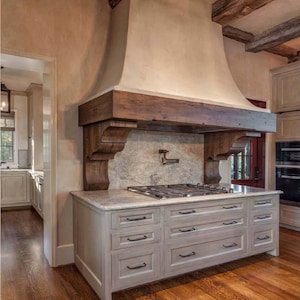 Könnte beinhalten: Eine weiße Kücheninsel mit einer Landhaus-Dunstabzugshaube und einem Gasherd. Die Insel hat sechs Schubladen mit schwarzen Griffen und einer weißen Arbeitsplatte.