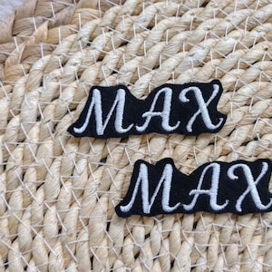 May include: Two black fabric patches with white embroidered lettering spelling out the name "MAX".