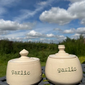 May include: Two white ceramic garlic jars with lids. The jars are labelled "garlic" in green lettering.