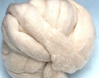 May include: A large, off-white bundle of wool roving, tightly coiled and knotted. The wool appears soft and fluffy, with visible fibers and a slightly textured surface. The background is a light blue.