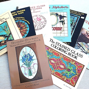 May include: A collection of stained glass pattern books, including titles like "Wildlife Images," "Stained Glass Window Art," and "Decorative Doorways." The books feature colorful illustrations and designs for various stained glass projects.