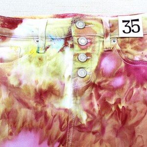 Könnte beinhalten: Eine Jeans in Tie-Dye-Optik in den Farben Pink, Gelb und Orange mit einem Größenetikett mit der Aufschrift "35".