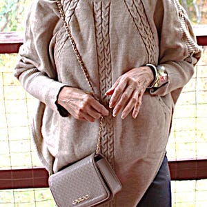 May include: A tan cable-knit poncho sweater with a turtleneck and a small, textured, rectangular purse with a gold chain strap. The purse has the word "bebe" in gold lettering. The sweater has a cable knit design down the front.