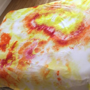 May include: A white fabric sheet with a tie-dye pattern in shades of yellow, orange, and red.