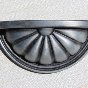 May include: A silver and black metal cabinet pull with a scalloped design.