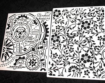 May include: Two white stencils with black designs. One features gears, a compass, and text including "navigation" and "figure 15." The other has a floral pattern with flowers and leaves. Both are on a black surface.