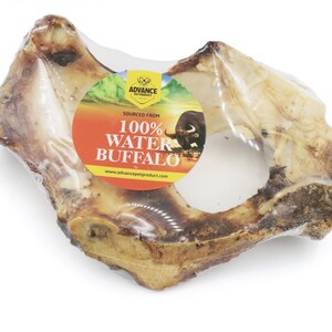 May include: A close-up of a large, light brown water buffalo bone chew wrapped in clear plastic. The label reads "Sourced From 100% Water Buffalo" with a picture of a buffalo.