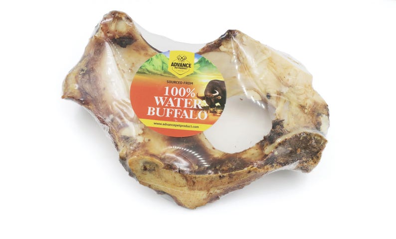 May include: A close-up of a large, light brown water buffalo bone chew wrapped in clear plastic. The label reads "Sourced From 100% Water Buffalo" with a picture of a buffalo.