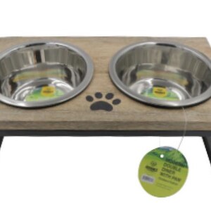 May include: A double diner pet bowl set with two stainless steel bowls set into a light brown wooden frame. The frame has a black paw print and is supported by black metal legs. A green tag hangs from the bowl.