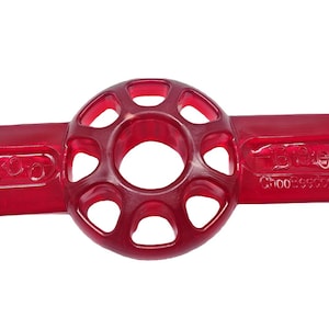 Può includere: Un giocattolo per cani in plastica rossa trasparente. Presenta una sezione circolare centrale con fori, collegata a due barre orizzontali con estremità arrotondate. Il testo "Dingo" e "Choo:56203" sono visibili.