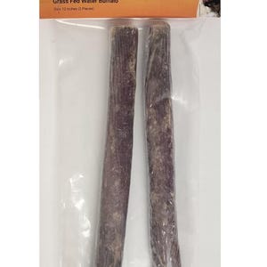 May include: A package of two 12-inch long, dark-colored, dried esophagus dog treats. The packaging includes text that reads "Pizzle Stuffed Esophagus" and "All Natural Water Buffalo Pet Treat". The treats are made from free-range, grass-fed water buffalo.