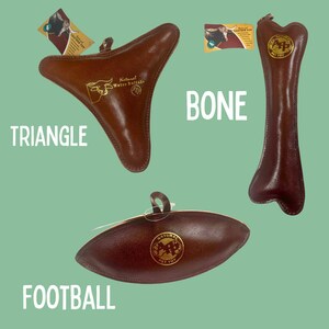 May include: Three leather dog toys in different shapes: a triangle, a bone, and a football. The toys are brown and have a gold logo that says "Natural Water Buffalo Pet Toy".