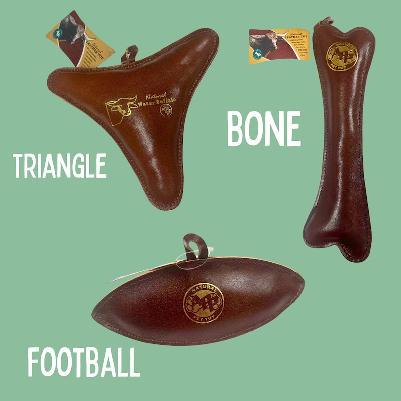 May include: Three leather dog toys in different shapes: a triangle, a bone, and a football. The toys are brown and have a gold logo that says "Natural Water Buffalo Pet Toy".
