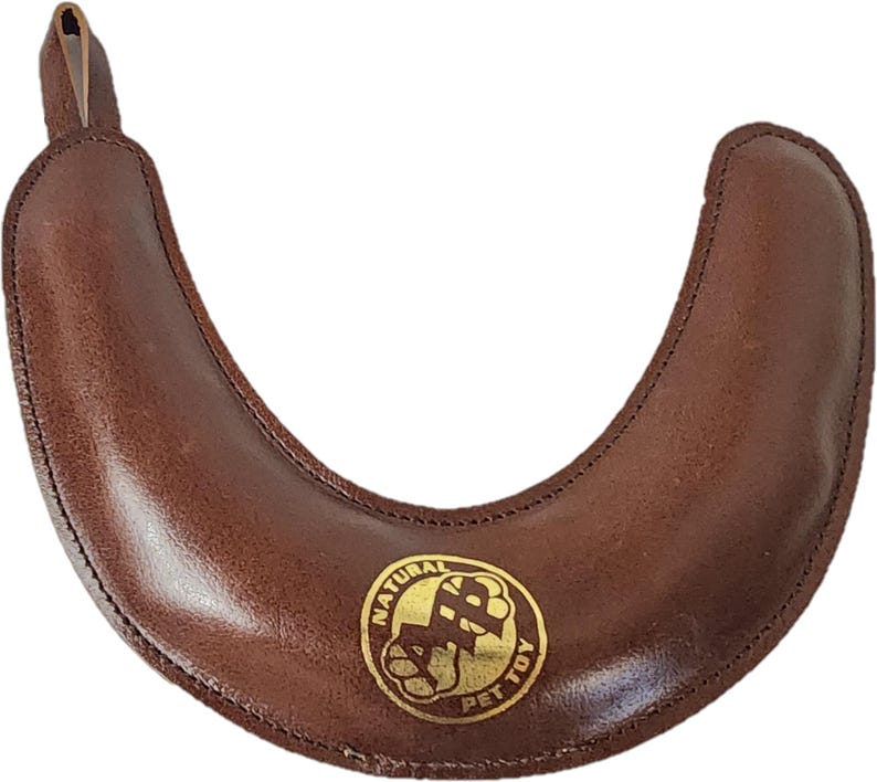 May include: Brown leather dog chew toy shaped like a horseshoe with a gold logo that says "Natural Pet Toy".