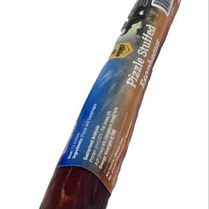 May include: A dark brown, cylindrical dog treat labeled "Pizzle Stuffed Esophagus." The treat is approximately 12 inches long. The label includes guaranteed analysis information: protein (min) 50%, fat (max) 6%, ash (max) 4%, and moisture (max) 10%.