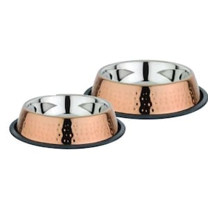 May include: Two copper-colored pet bowls with a hammered texture and stainless steel interiors. Each bowl sits on a black rubber base. The bowls are designed for pet food or water.