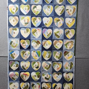 May include: A quilt made of denim fabric with a patchwork design of hearts. Each heart is made of different colored fabrics and has a white outline. The quilt is a light blue color with a white border.