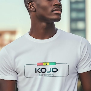 Könnte beinhalten: Weißes T-Shirt mit Rundhalsausschnitt und dem Namen "KOJO" in einem rechteckigen Design. Das Design enthält die Farben der ghanaischen Flagge und den Text "[MONDAY BORN]" darunter. Das T-Shirt wird von einer Person getragen.