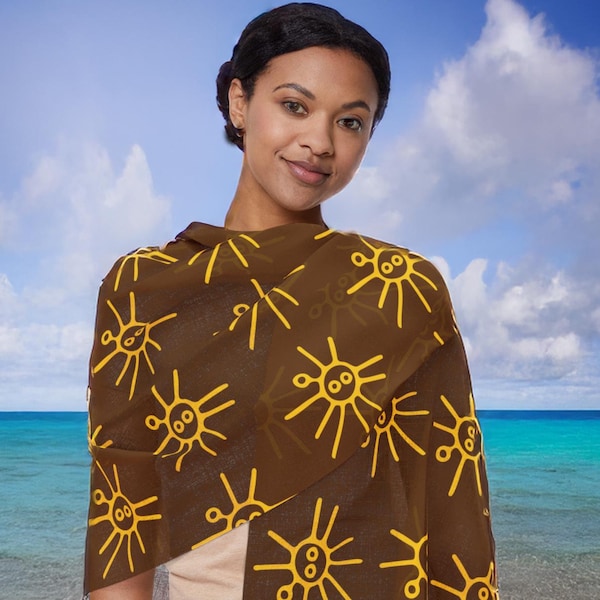 May include: A brown scarf with a yellow sun design. The scarf is worn by a person standing in front of a beach scene.