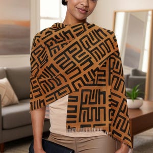 May include: A brown and black patterned scarf draped over the shoulders. The scarf features a repeating geometric design in black against a brown background. The scarf is fringed at the ends. A black clutch is held in the hand.