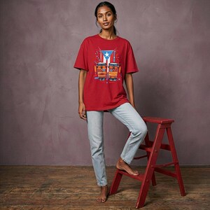 May include: A red t-shirt featuring a graphic of the Puerto Rican flag and two drums. The shirt is worn with light blue jeans. A red step stool is in the foreground.