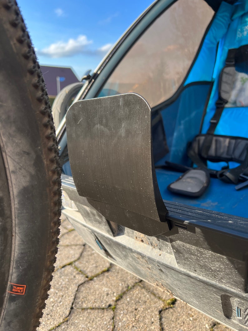 Puede incluir: Una solapa de pl&aacute;stico negro en un cochecito azul y gris. La solapa est&aacute; unida al cochecito con una bisagra y tiene una superficie lisa. La solapa est&aacute; cerrada y el cochecito est&aacute; estacionado en un camino de adoquines.