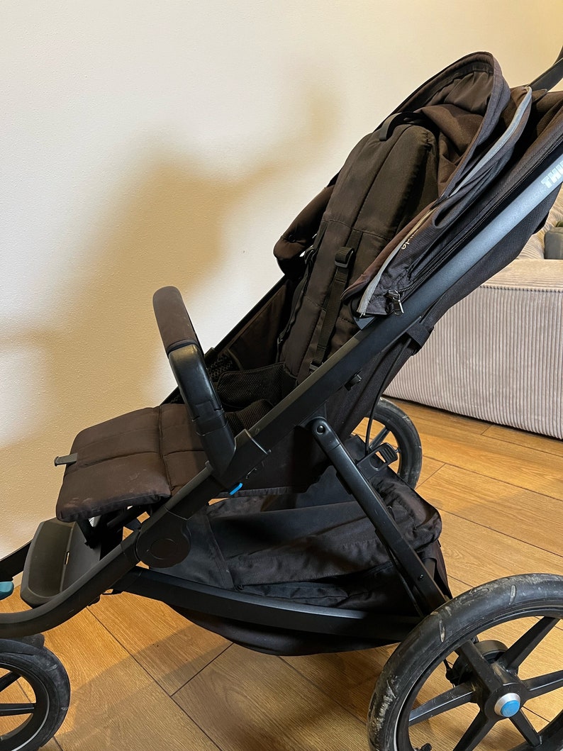 May include: A black stroller with a brown seat and a large storage basket. The stroller has a black canopy and a black handle.