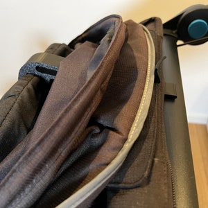 May include: Close-up of a black stroller canopy with a zipper and a reflective strip. The canopy is made of a water-resistant fabric.