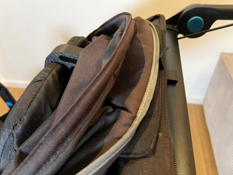 May include: Close-up of a black stroller canopy with a zipper and a reflective strip. The canopy is made of a water-resistant fabric.