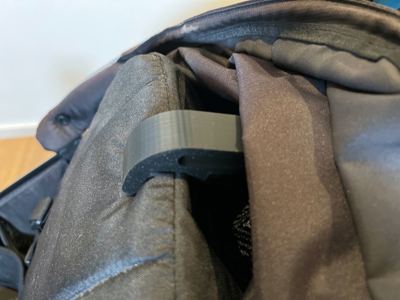 May include: A black plastic stroller hook with a rubberized grip. The hook is attached to the stroller canopy.