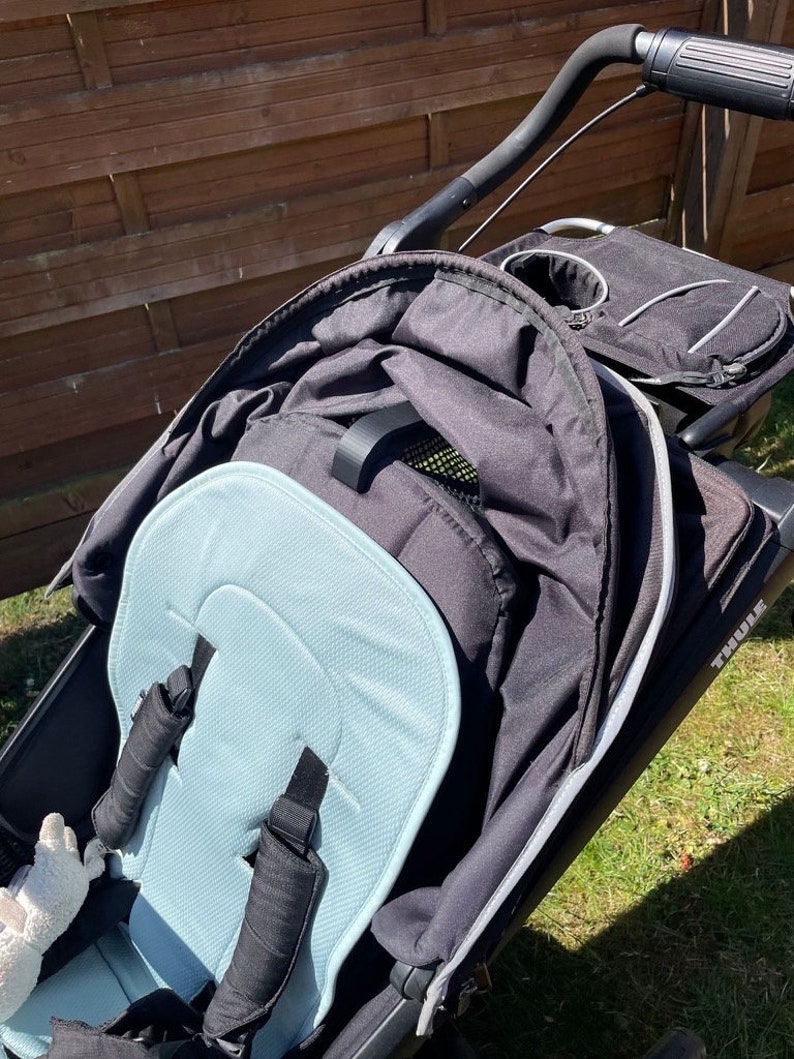 May include: A black stroller with a blue padded seat and a black canopy. The stroller has a cup holder and a storage basket. The Thule brand name is visible on the side of the stroller.