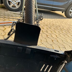 Puede incluir: Un portabicicletas negro fijado a la parte trasera de un coche plateado. El portabicicletas est&aacute; vac&iacute;o y tiene una solapa de metal negro que est&aacute; parcialmente abierta. El coche est&aacute; aparcado en una entrada de adoquines grises.