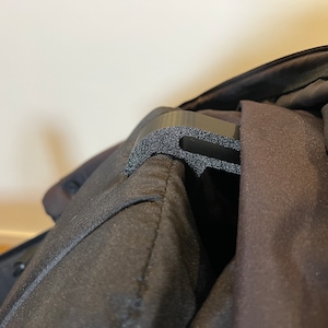 May include: A black plastic hook with a textured surface attached to a black fabric bag.