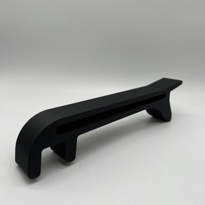 May include: A black plastic tool with a handle and a hook on the end. The tool is designed to help open cans.