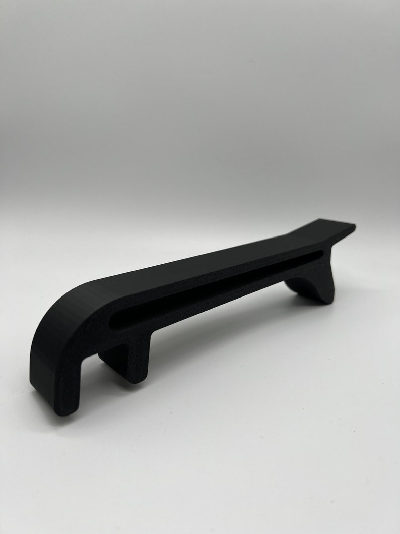 May include: A black plastic tool with a handle and a hook on the end. The tool is designed to help open cans.