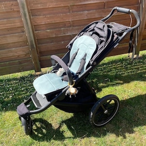 May include: A black stroller with a blue padded seat and a black canopy. The stroller has a single front wheel and two rear wheels. The stroller is on a grassy surface.
