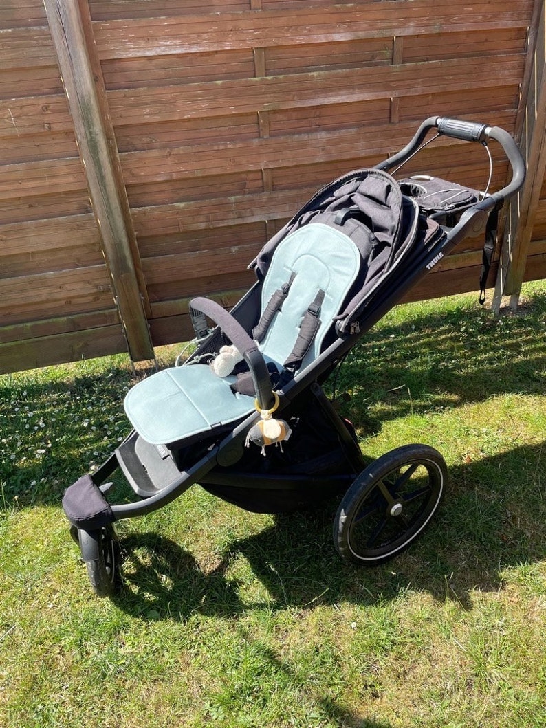 May include: A black stroller with a blue padded seat and a black canopy. The stroller has a single front wheel and two rear wheels. The stroller is on a grassy surface.