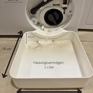 Può includere: Una vaschetta di drenaggio in plastica bianca per filtro di lavatrice, con una capacità di 1 litro. La vaschetta misura 18 cm per 18 cm con una profondità di 4,5 cm. È posizionata per raccogliere l'acqua dal foro del filtro di un elettrodomestico.